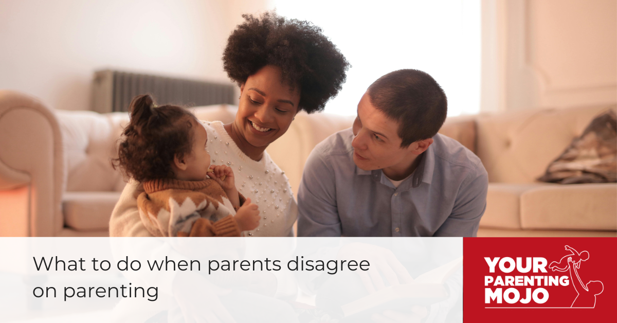 A smiling couple sits on a couch with their young child. The mother is holding the child while the father looks on attentively.