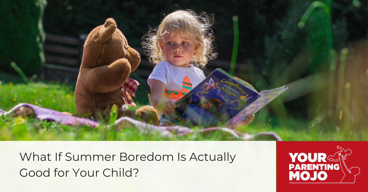 A young child with curly blonde hair sits on a picnic blanket outdoors, holding an open storybook while a brown teddy bear sits nearby