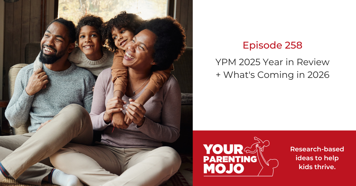 A happy family of four sits together on a couch - two parents and their two young children are smiling and embracing, with warm lighting coming through a window behind them